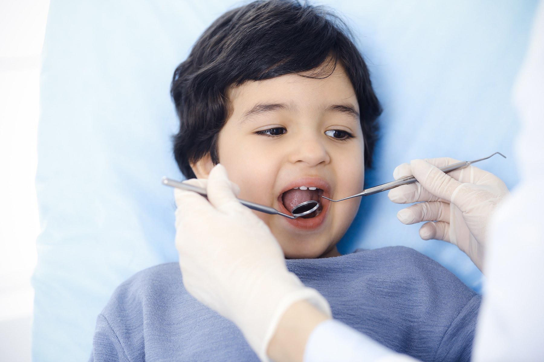 Cute arab boy sitting at dental chair with open mouth during oral checking up with doctor. Visiting dentist office. Stomatology concept