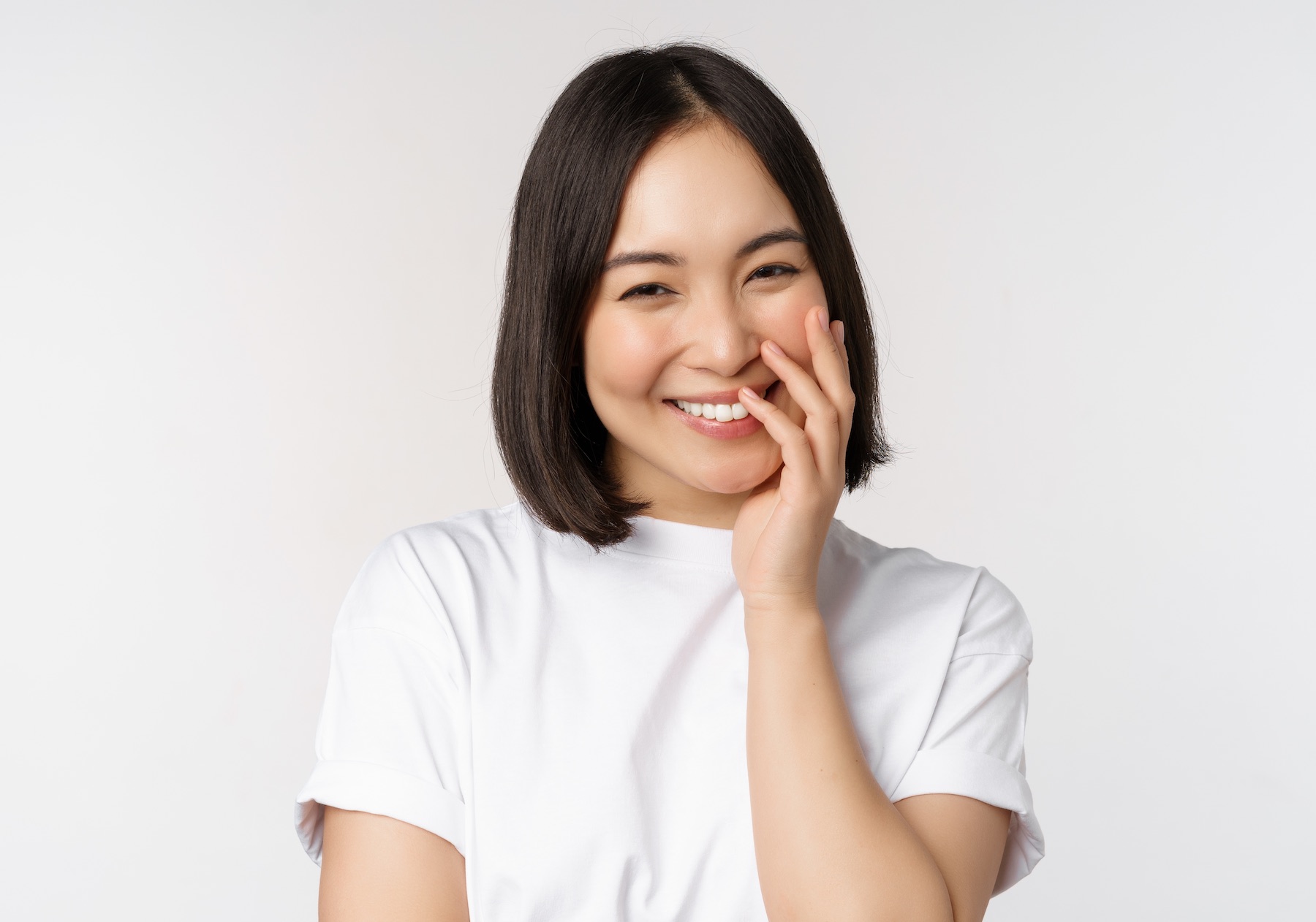 Portrait of young beautiful woman, korean girl laughing and smiling, looking coquettish, standing against white background